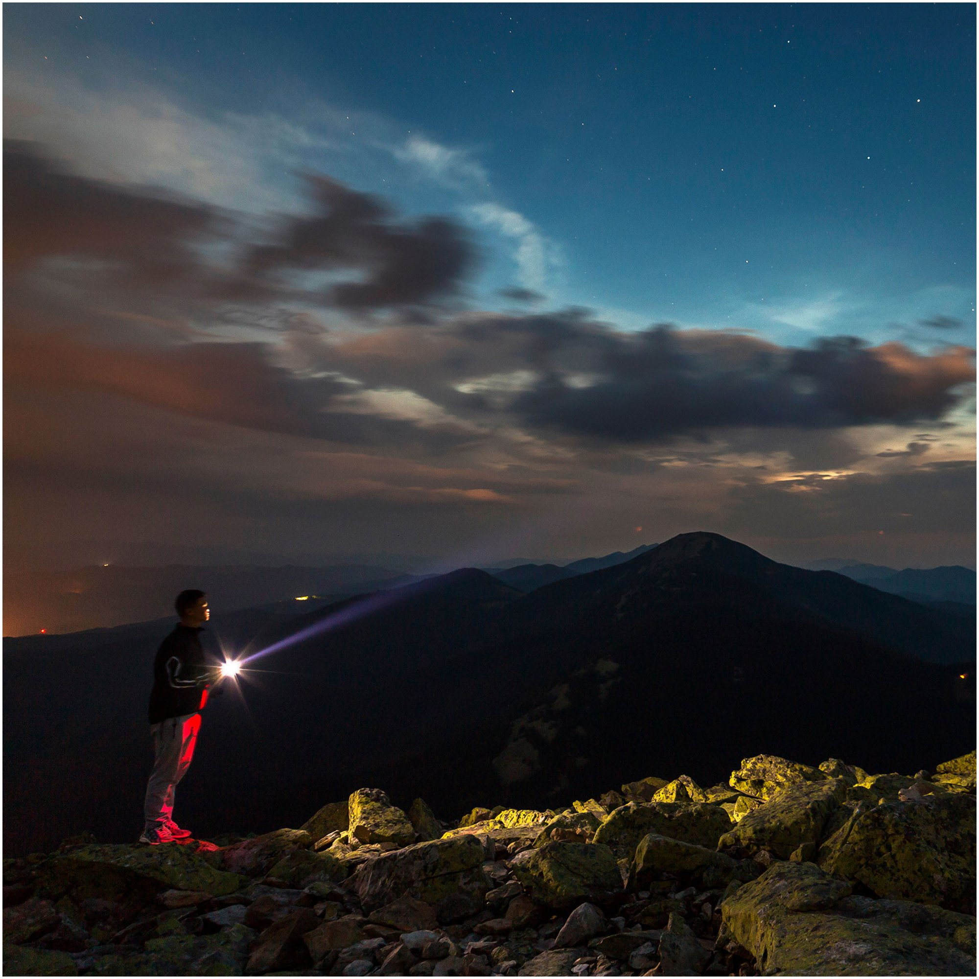 Eine Person leuchtet mit einer Taschenlampe über Berge unter nächtlichem Sternenhimmel.