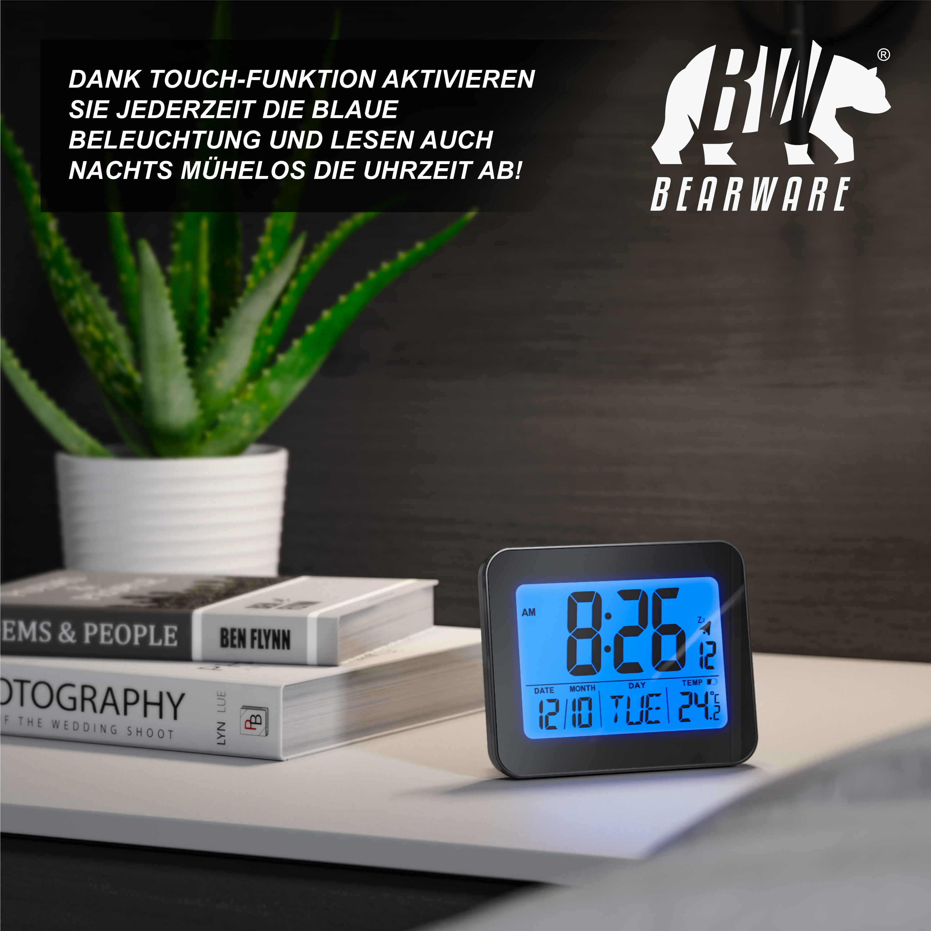 Ein schwarzer Digitalwecker mit blauem Display steht auf einem Tisch neben Büchern und einer Topfpflanze.