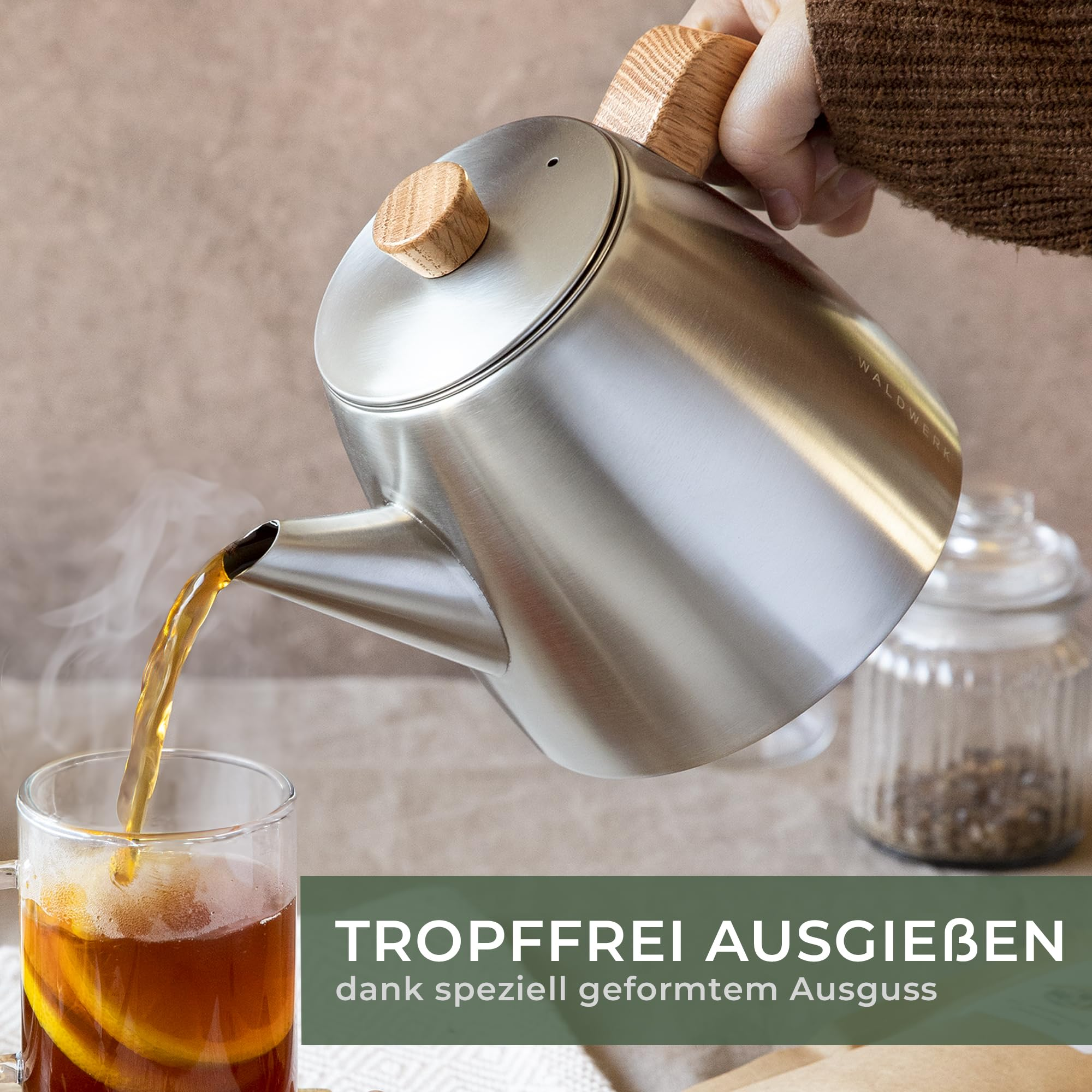 Eine Hand giesst Tee aus einer Edelstahlkanne mit Holzgriffen in ein Glas.