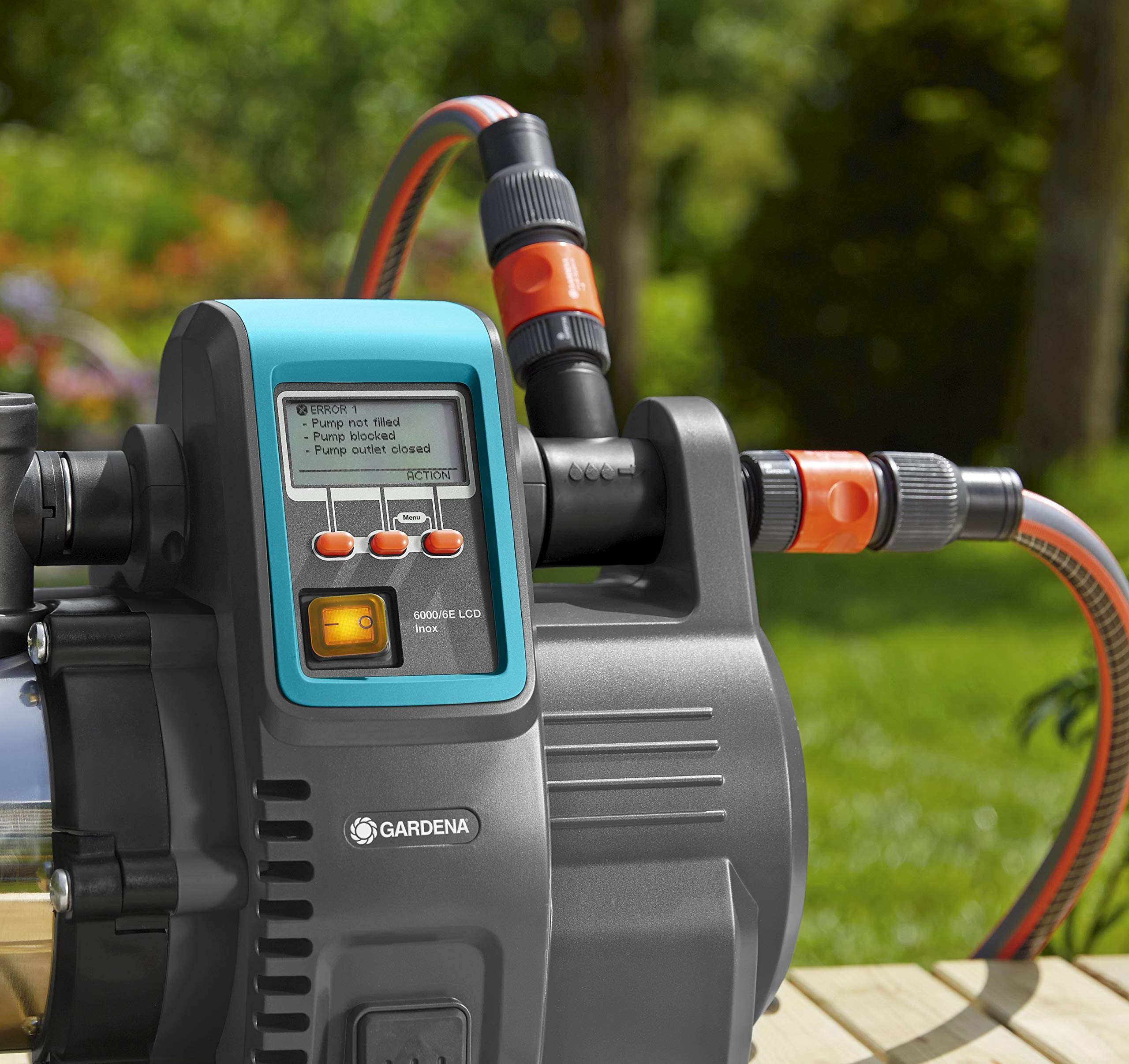 Gardena Gartenpumpe mit LCD-Display und angeschlossenen Schläuchen auf Holztisch in grünem Garten.