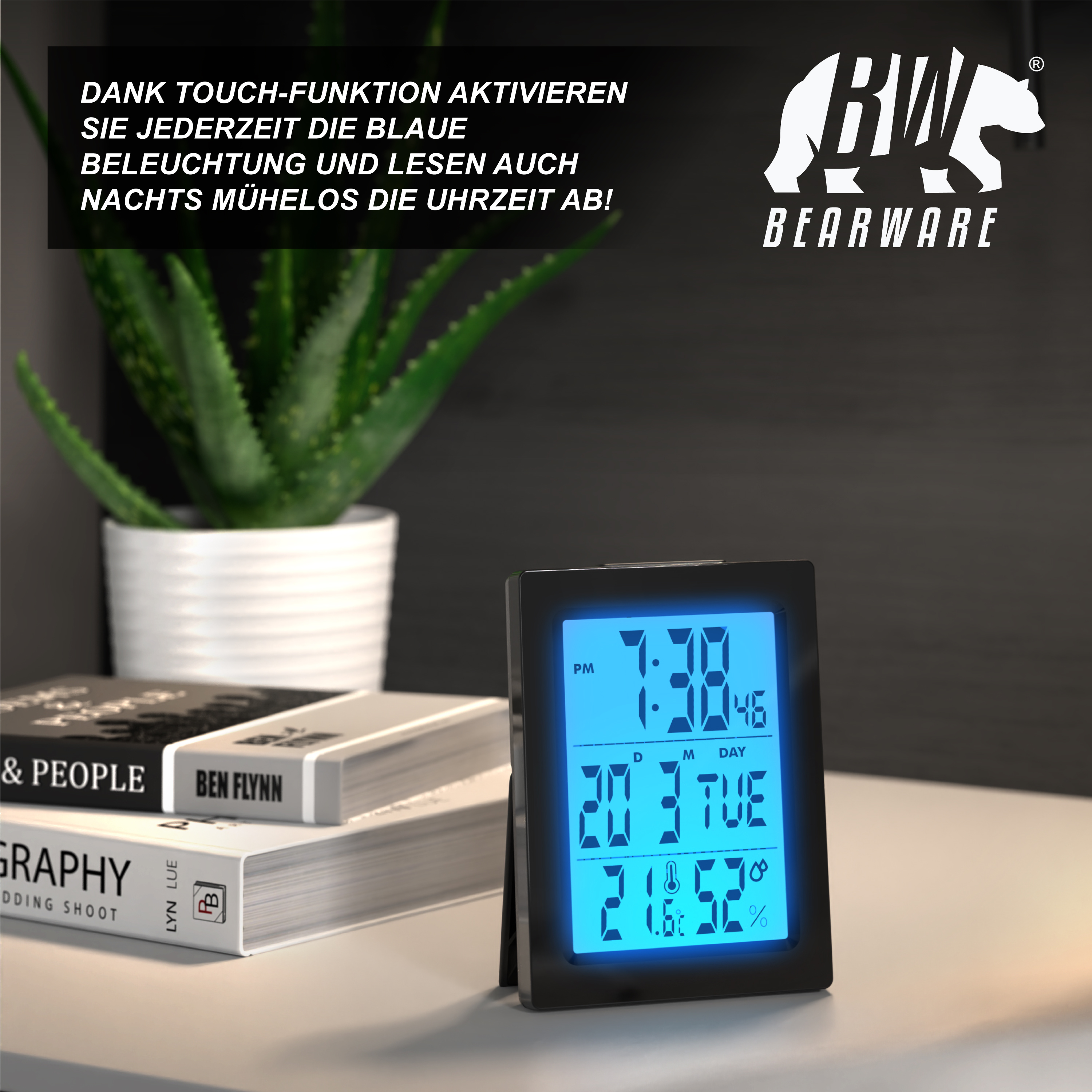 Digitale Uhr mit blauem Display auf einem Tisch, daneben Bücher und eine Topfpflanze.