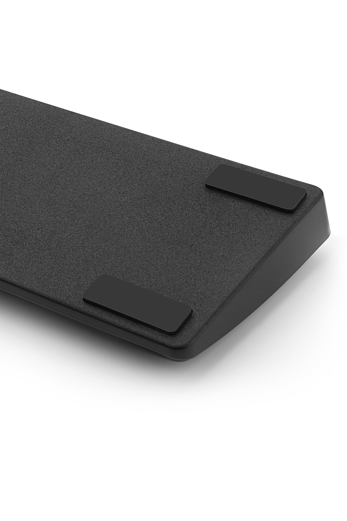 La parte inferior de un teclado negro con dos patas de goma negras rectangulares sobre un fondo blanco.