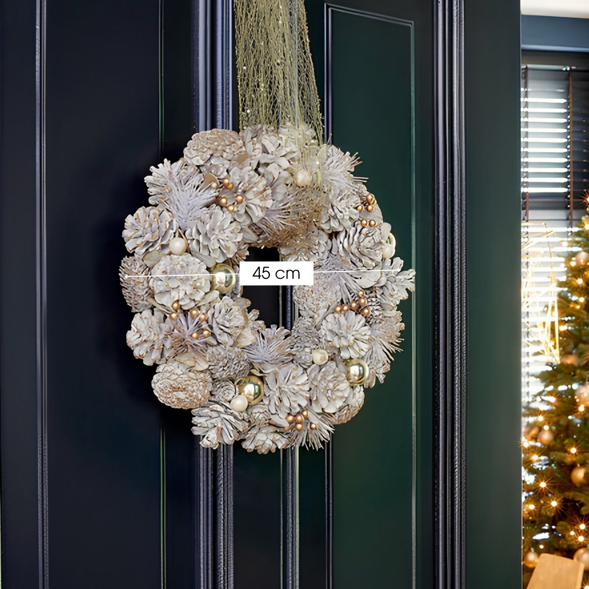 Une couronne décorative de 45 cm en pommes de pin blanches et ornements dorés accrochée à une porte sombre.