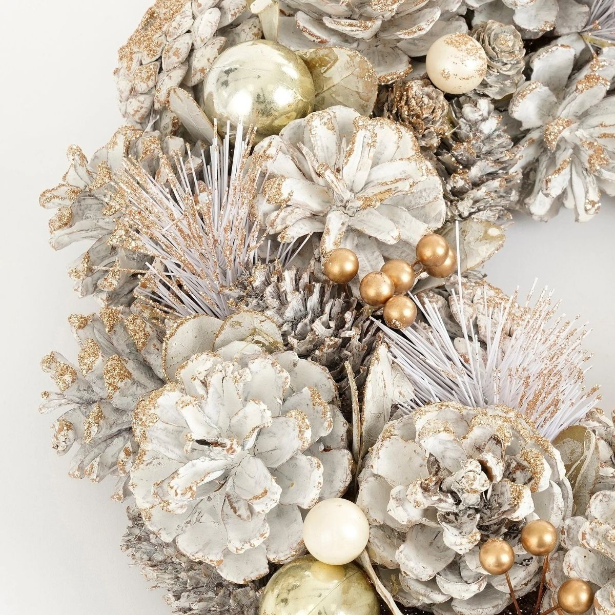 Une décoration de couronne de Noël blanche et dorée avec des pommes de pin.