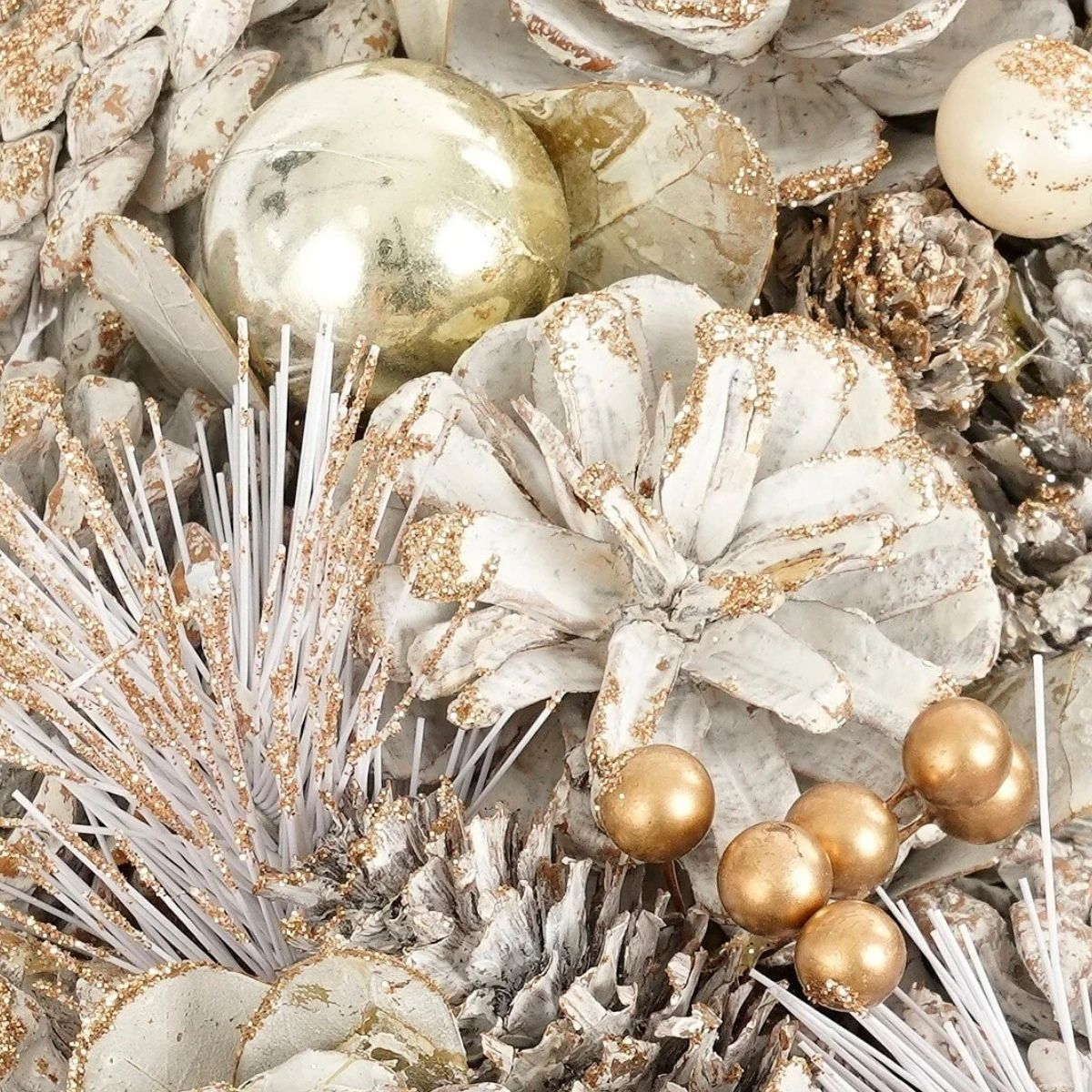 Décoration de Noël avec des pommes de pin blanches, des boules dorées et des branches pailletées.