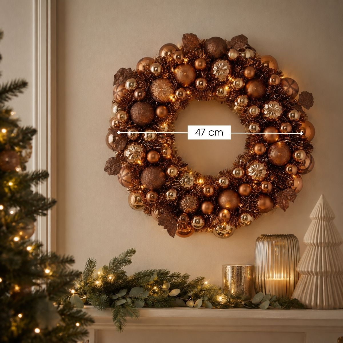 A bronze Christmas wreath with baubles and lights hangs on a wall above a decorated mantelpiece.