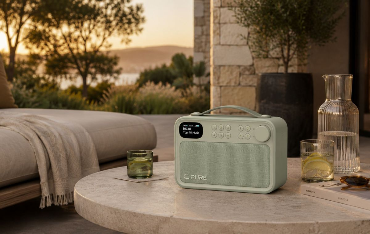 Una radio verde sobre una mesa de piedra al aire libre, con vasos de bebidas y un libro al atardecer.