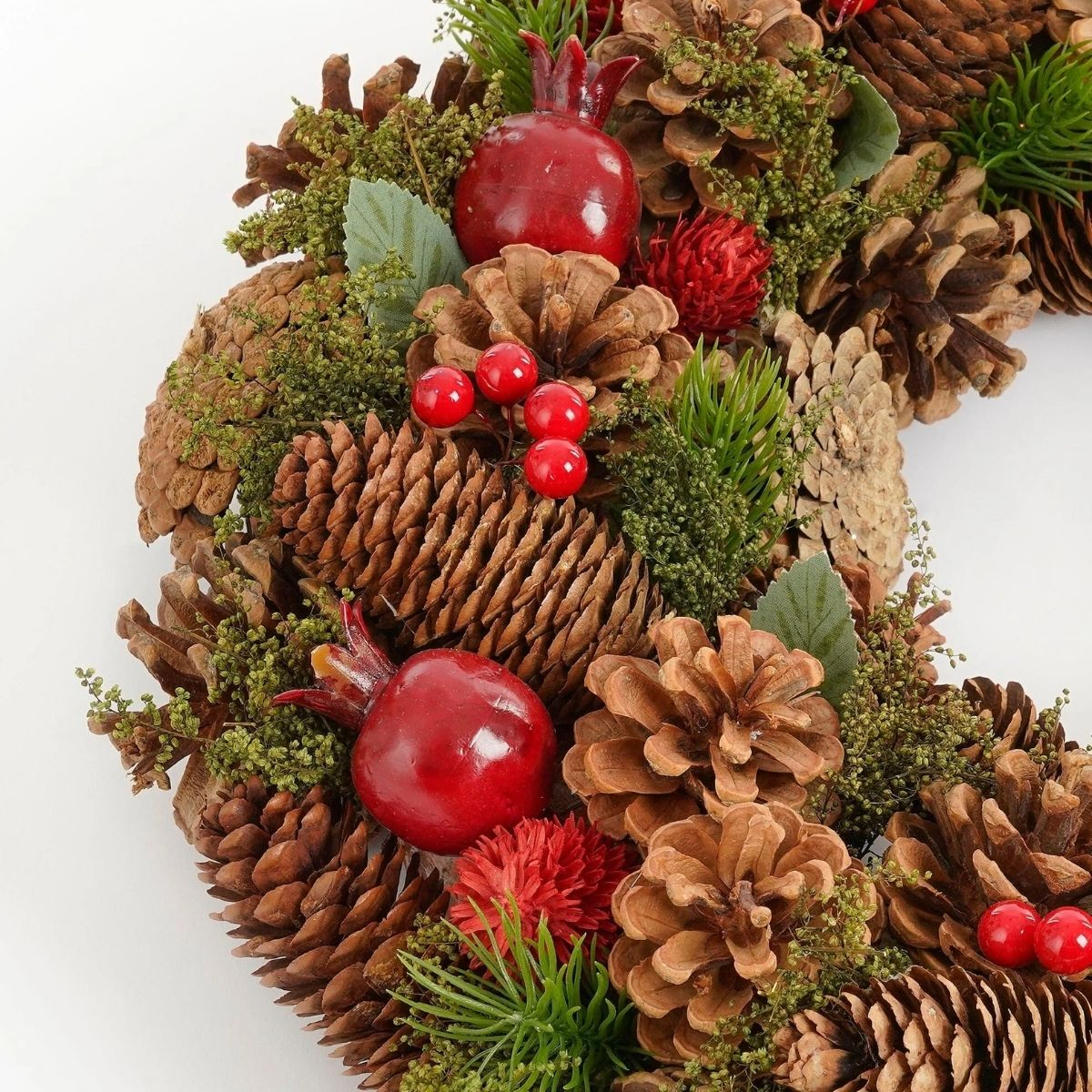 A festive wreath with pinecones, red pomegranates, green foliage, and red berries on a white background.