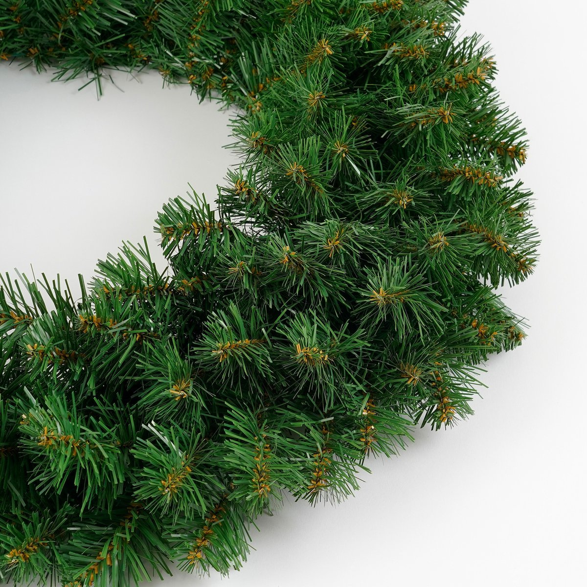 A dense artificial pine wreath lies on a white background.