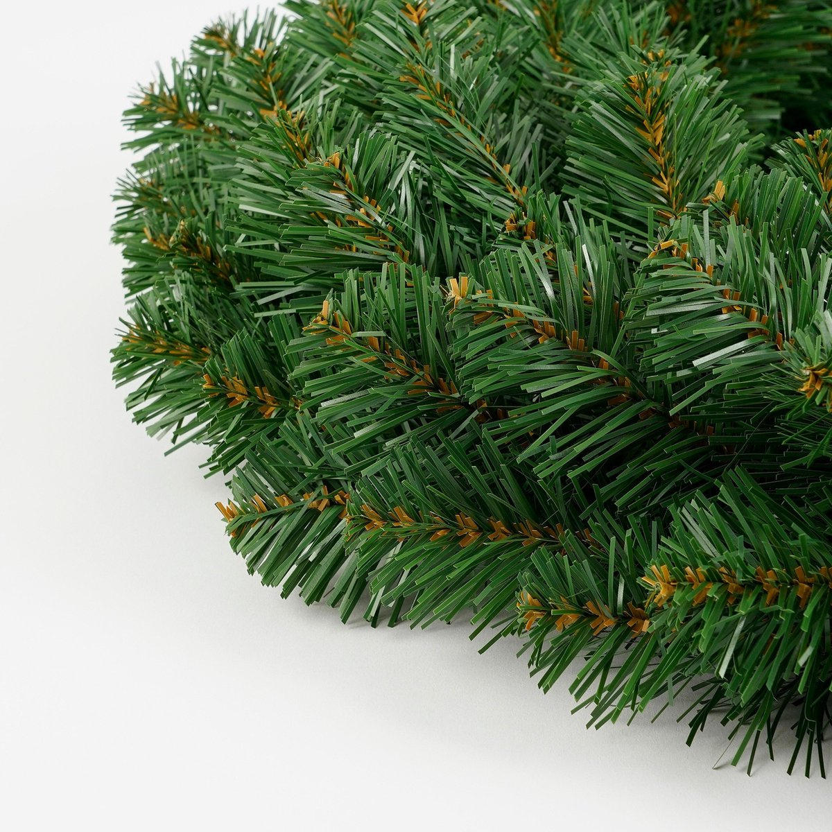 Close-up of an artificial green fir Christmas wreath against a white background.