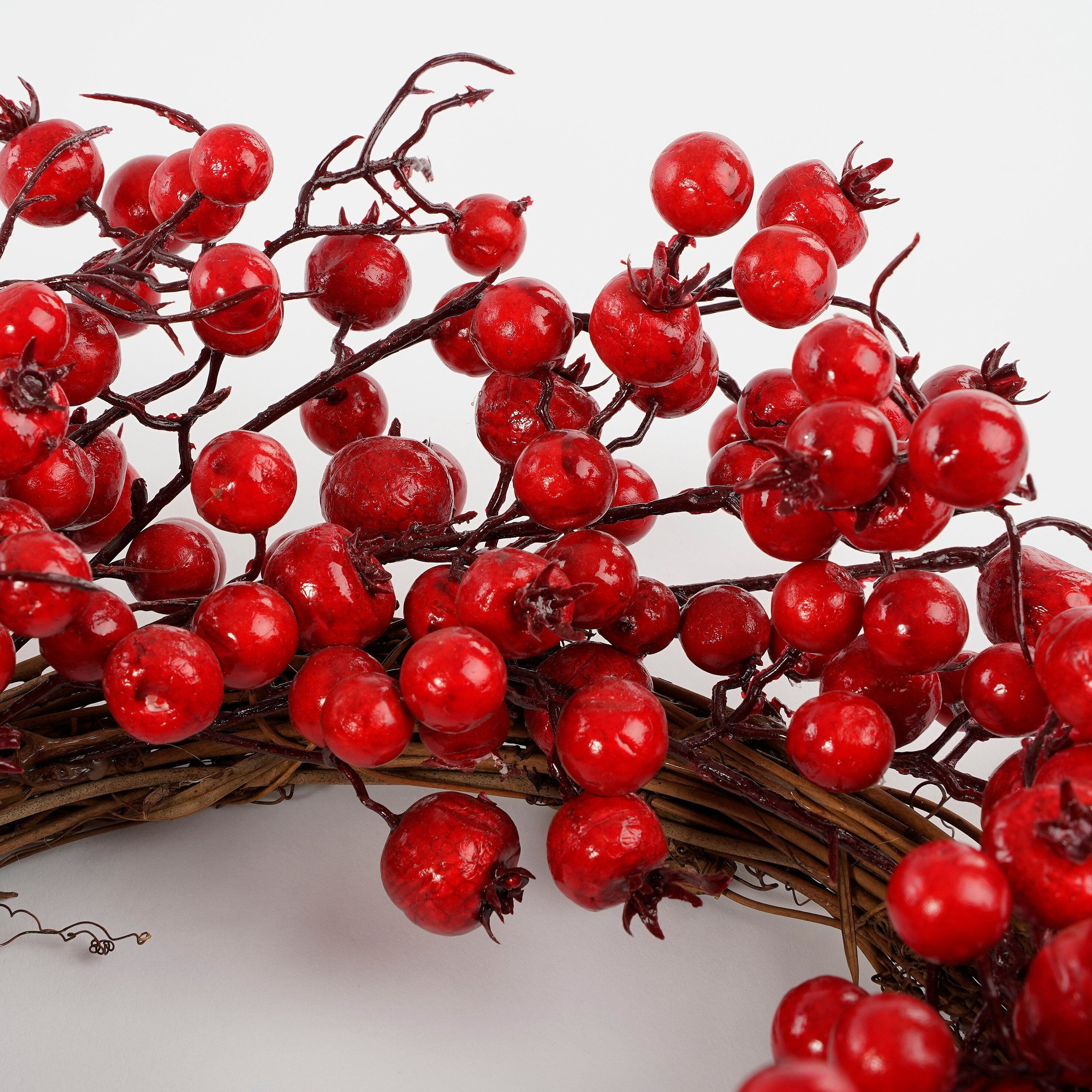 A decorative wreath made of twigs and clusters of shiny red berries against a white background.