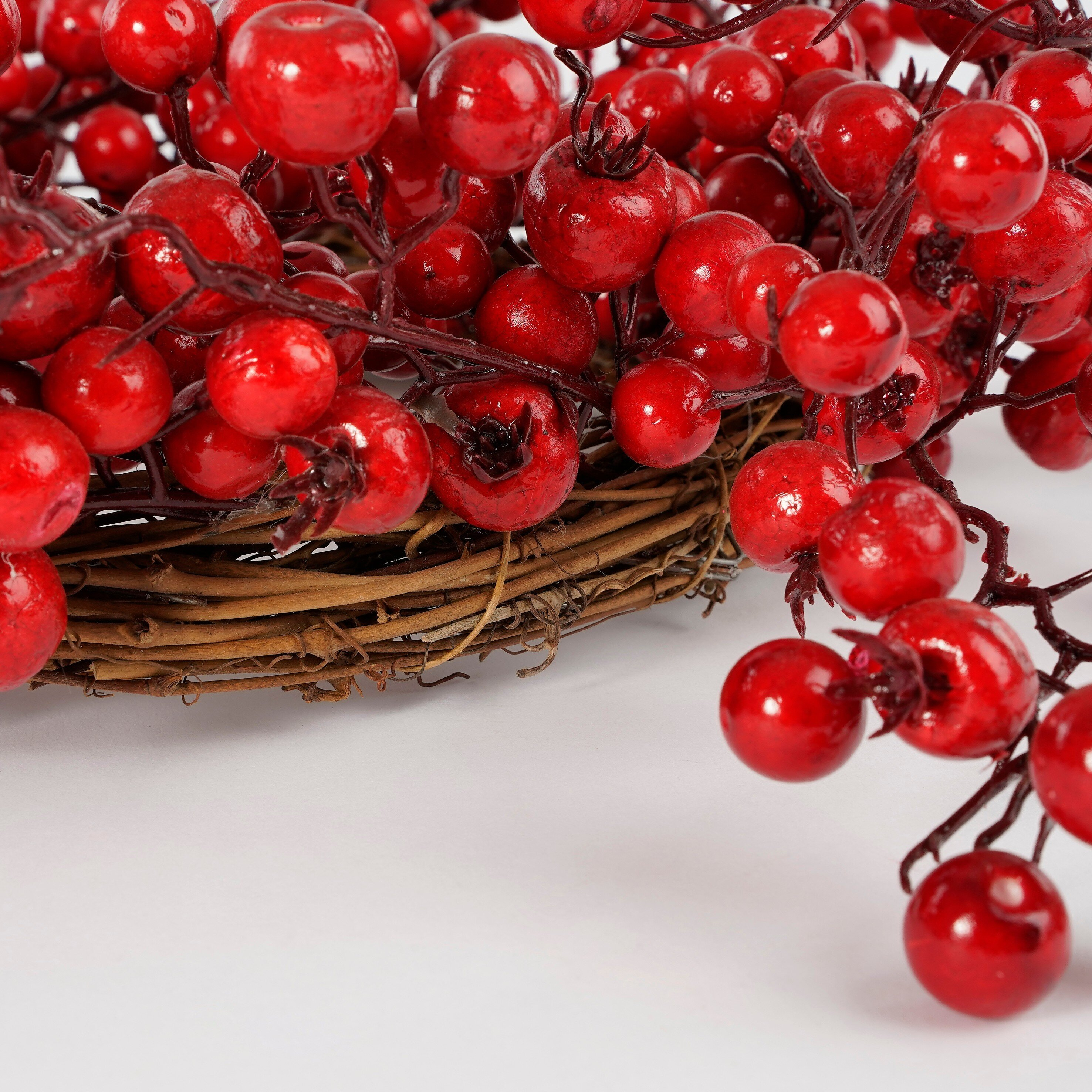 A wreath of brown twigs, densely covered with bright red berries, on a light background.