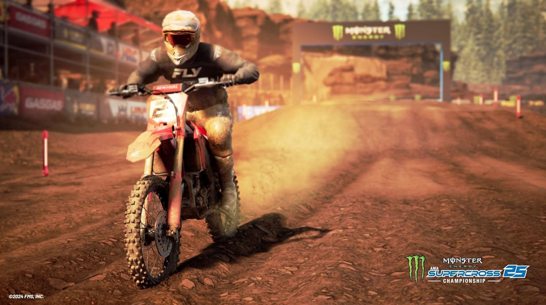 Un motociclista de motocross en una moto roja corre en una pista polvorienta con una puerta de salida al fondo.