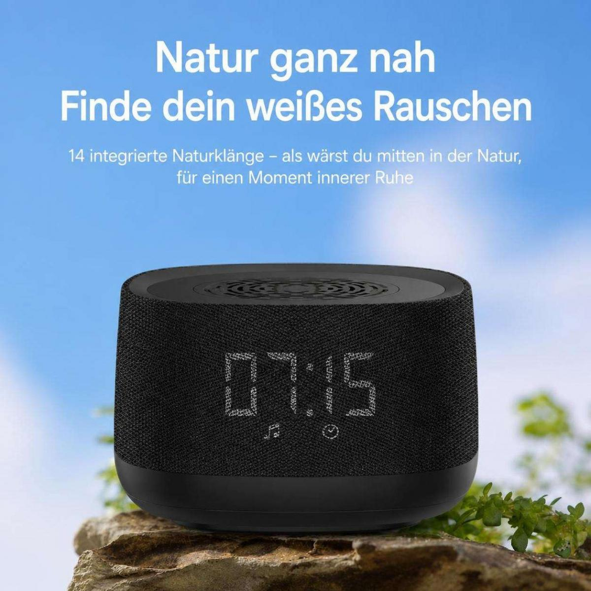 Ein schwarzer Lautsprecher mit digitaler Zeitanzeige auf Moos und Stein vor blauem Himmel.