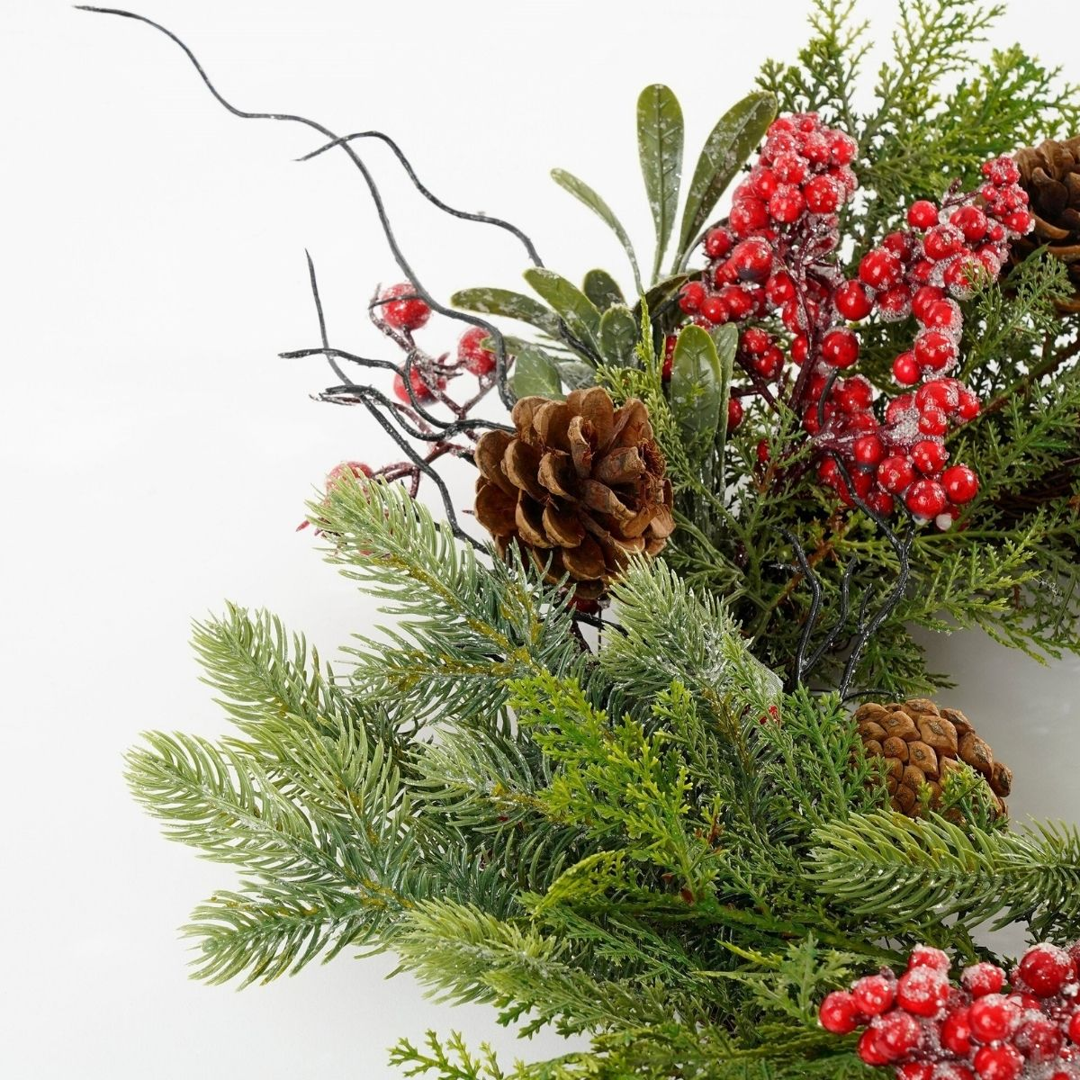 A festive wreath with green pine branches, red berries, pinecones, and dark twisted twigs on white.