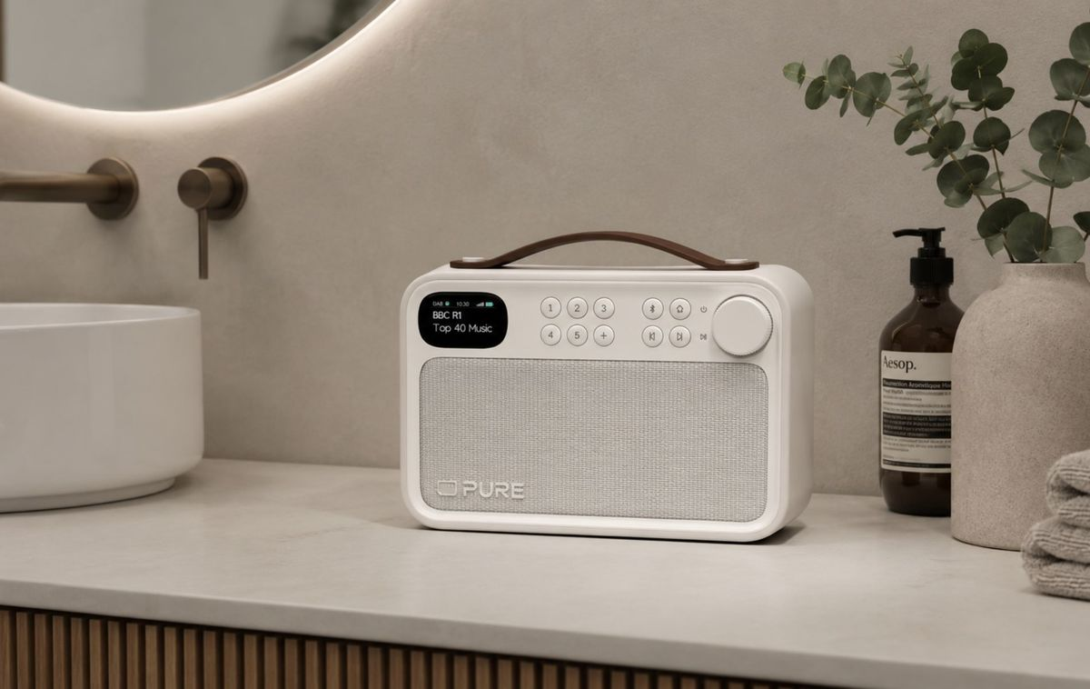 Una radio Pure blanca con asa de cuero está en el tocador de un baño, junto a un lavabo.