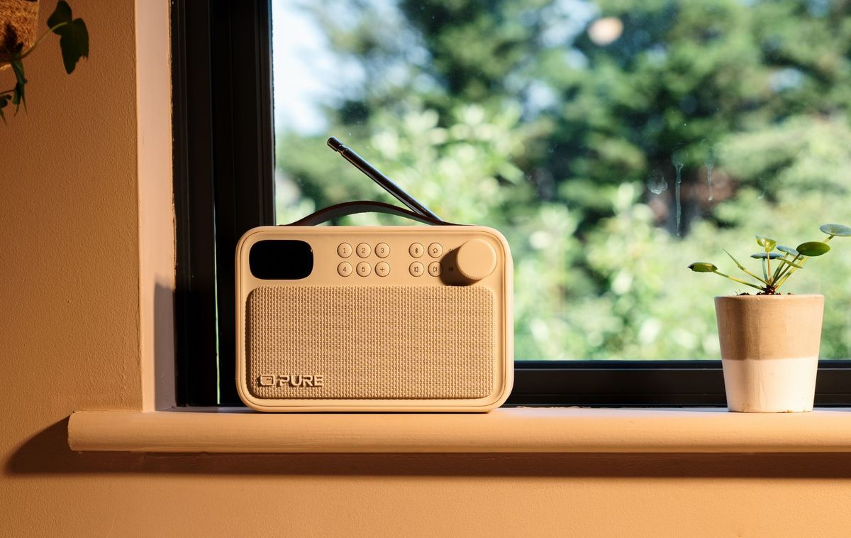 Un receptor de radio beige se encuentra en el alféizar de una ventana junto a una pequeña planta en maceta.