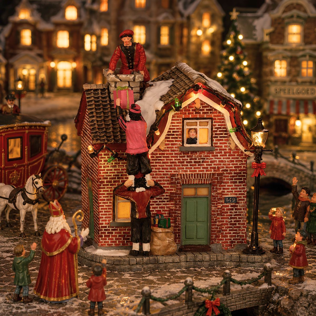 Minidorf-Szene: Sinterklaas sieht zu, wie Personen Geschenke auf einem Ziegelhaus stapeln.