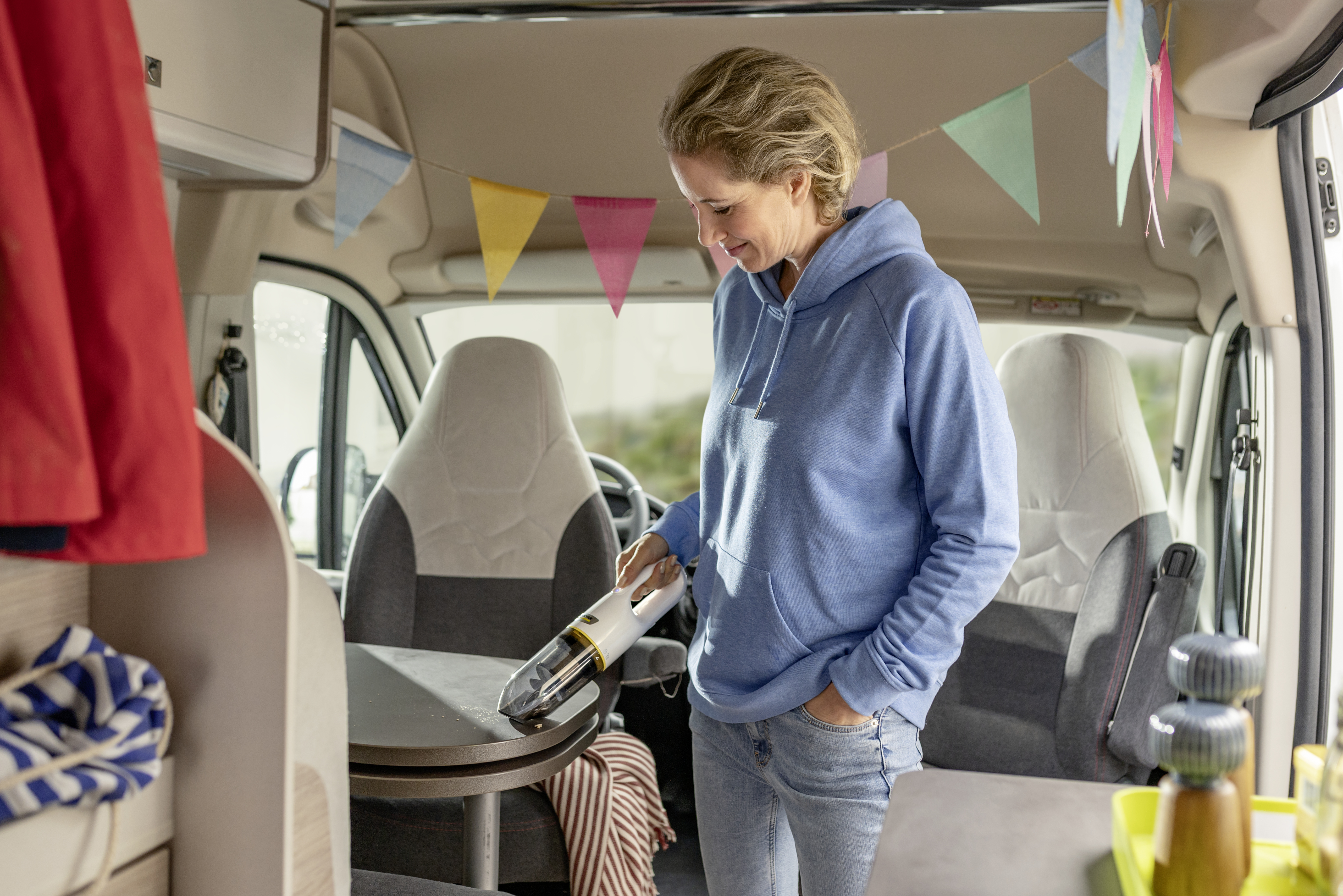 Una donna con una felpa blu passa l'aspirapolvere sul tavolo di un camper.