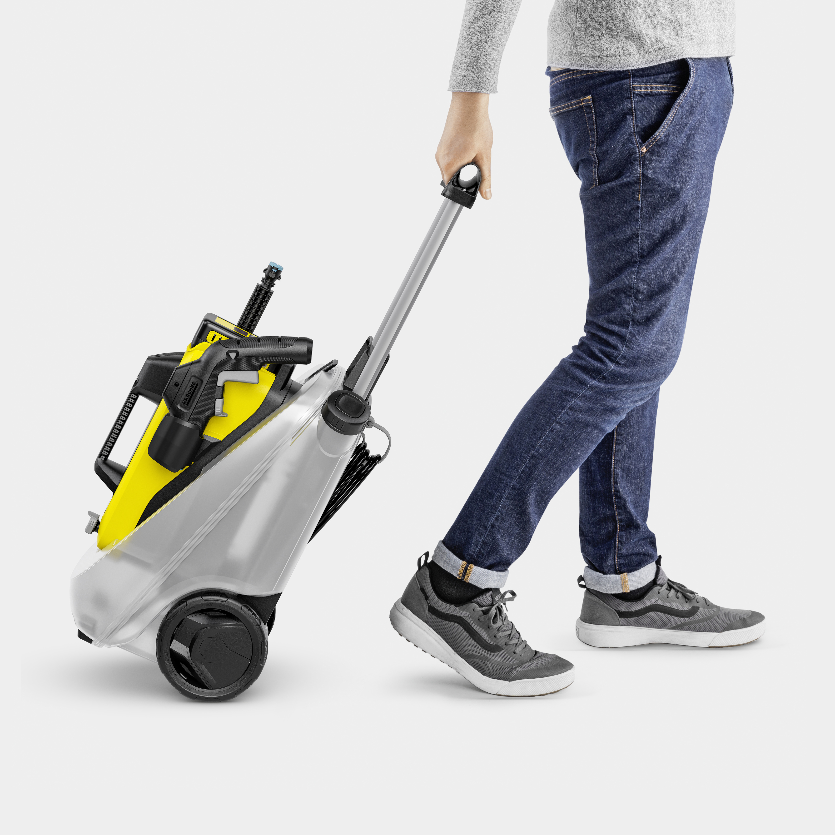 Eine Person in Jeans und Sneakers zieht einen gelb-grauen Hochdruckreiniger auf Rädern.