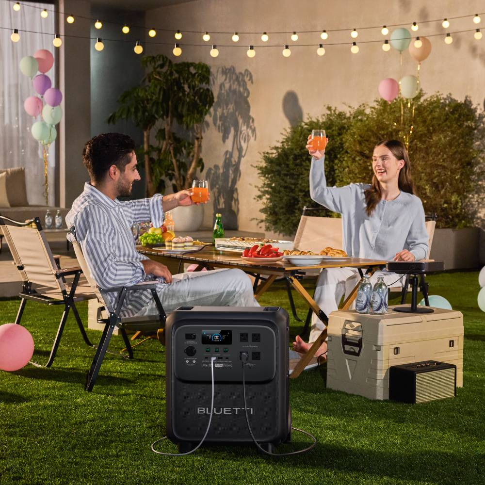 Ein Paar stößt bei einer Gartenparty mit Saft an, im Vordergrund auf dem Gras steht eine Bluetti-Powerstation.