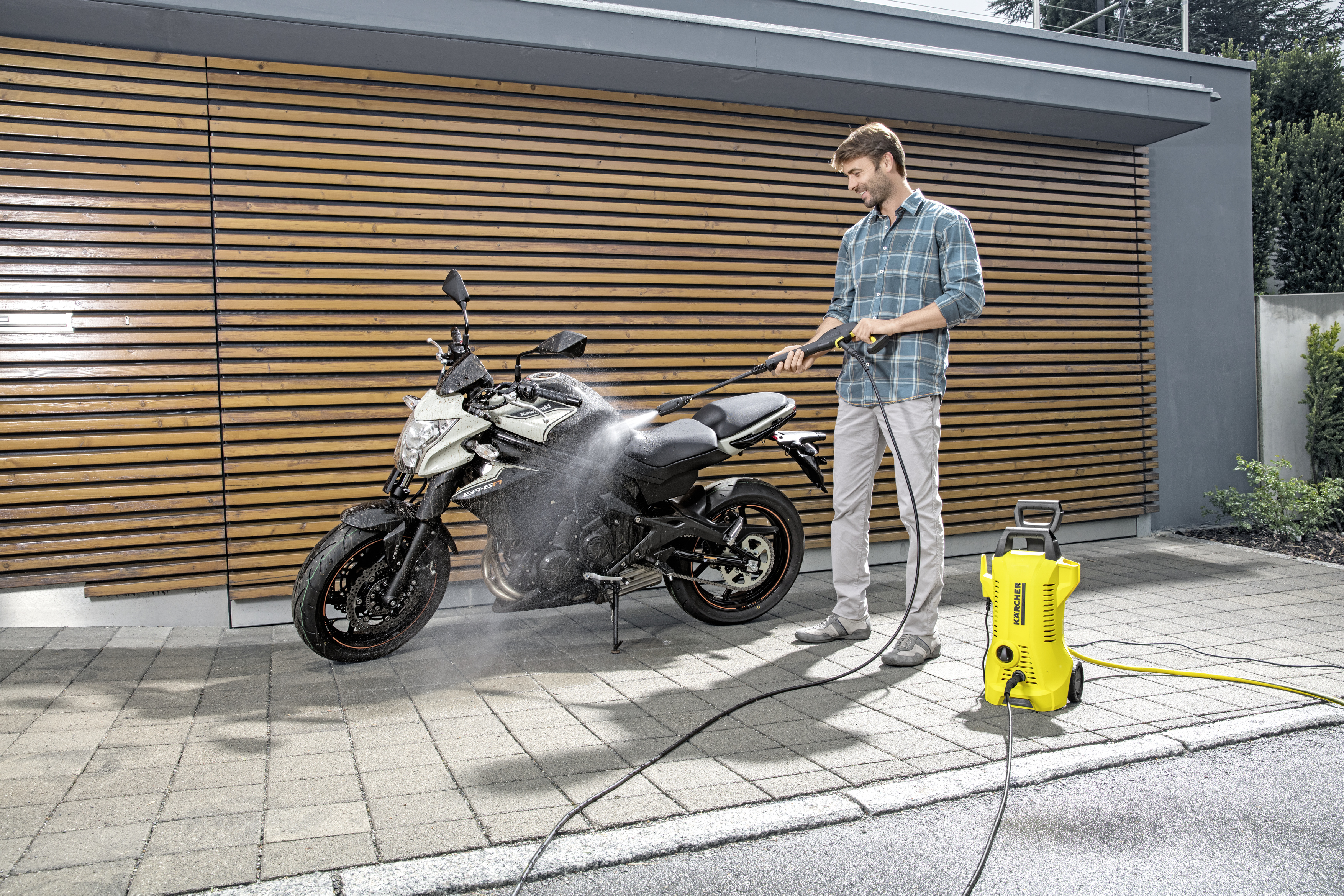 Ein Mann wäscht ein schwarzes Motorrad mit einem gelben Hochdruckreiniger.