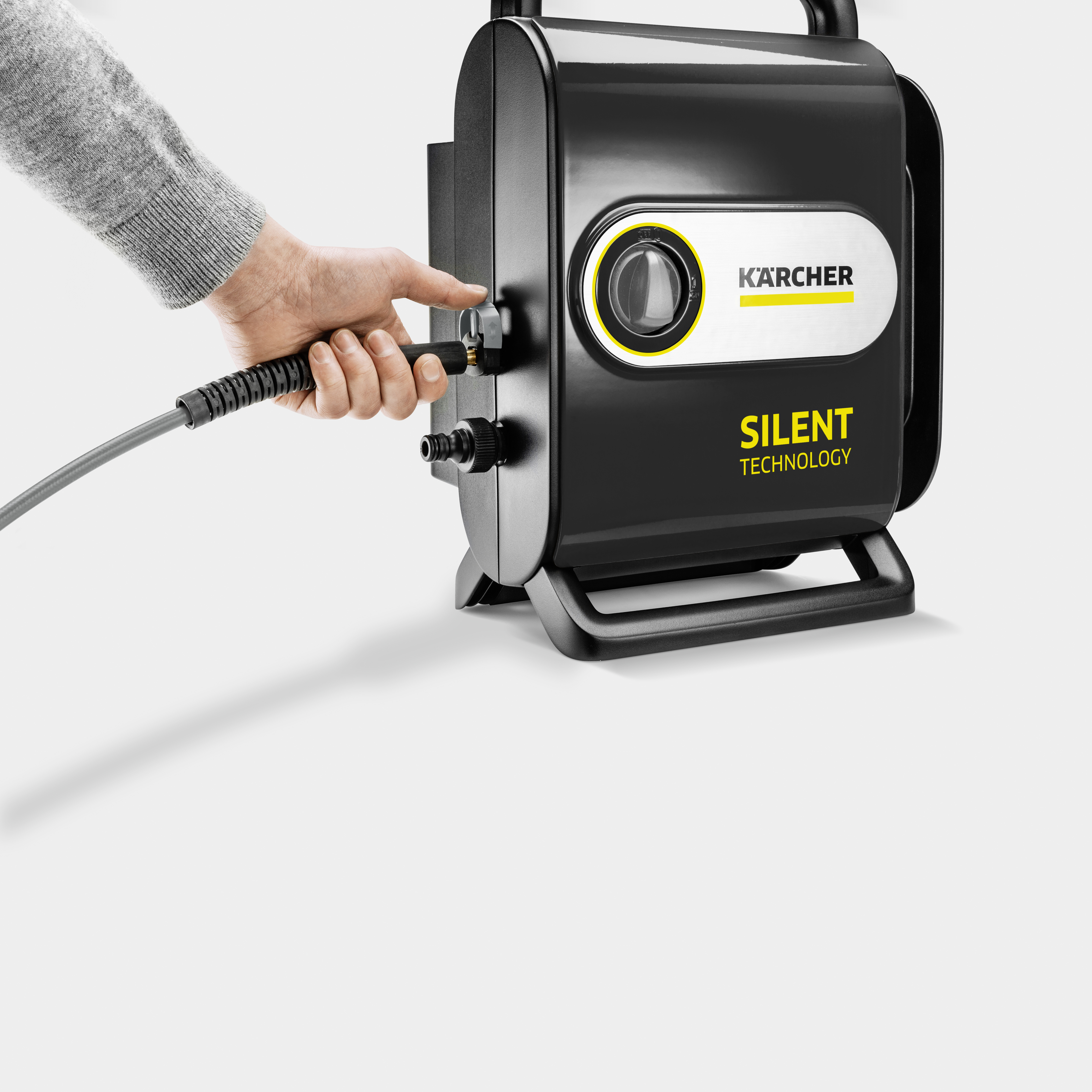 Eine Hand schließt einen Schlauch an einen schwarzen Kärcher Hochdruckreiniger mit der Aufschrift Silent Technology an.