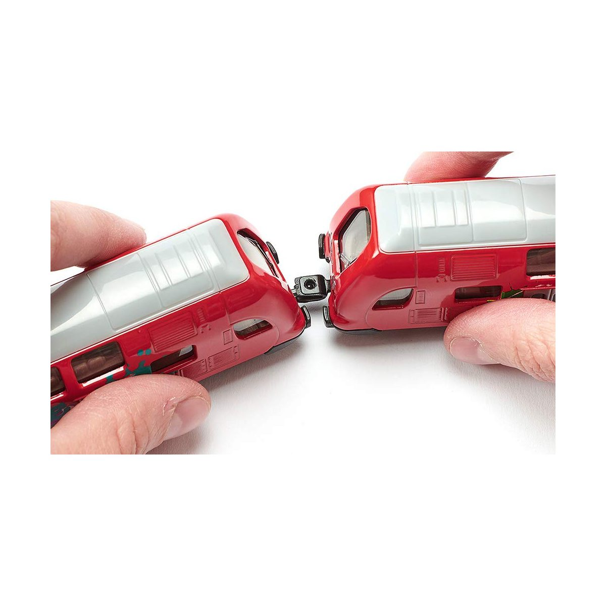 Hände verbinden zwei rote Spielzeugeisenbahnwaggons vor weißem Hintergrund.