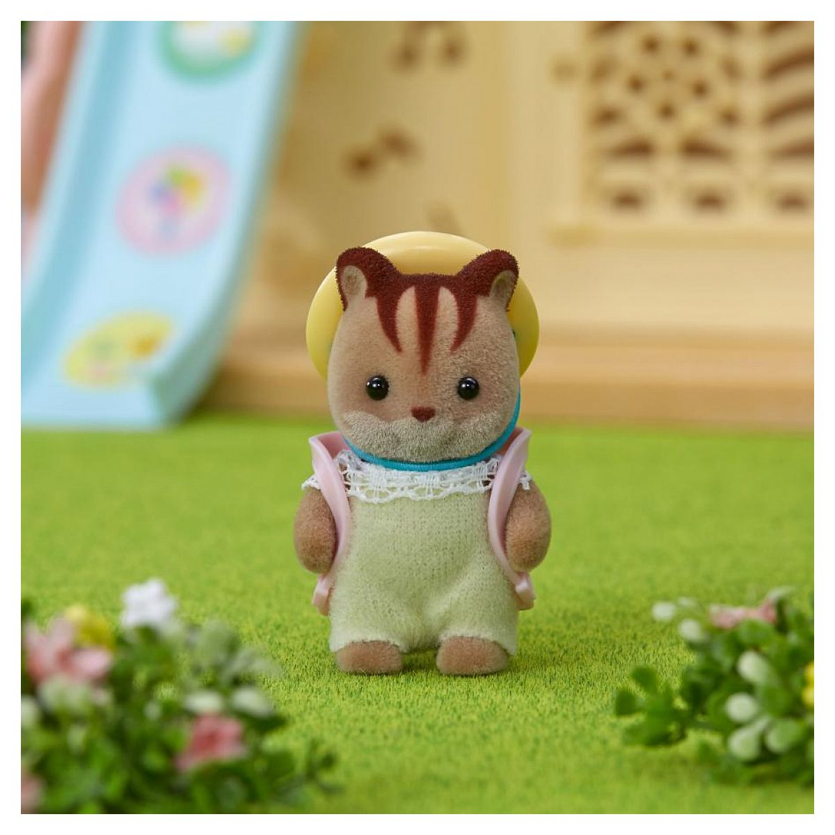 Eine flauschige Streifenhörnchen-Figur mit grünem Latzhose, weißem Spitzenkragen und gelbem Hut steht im Gras.