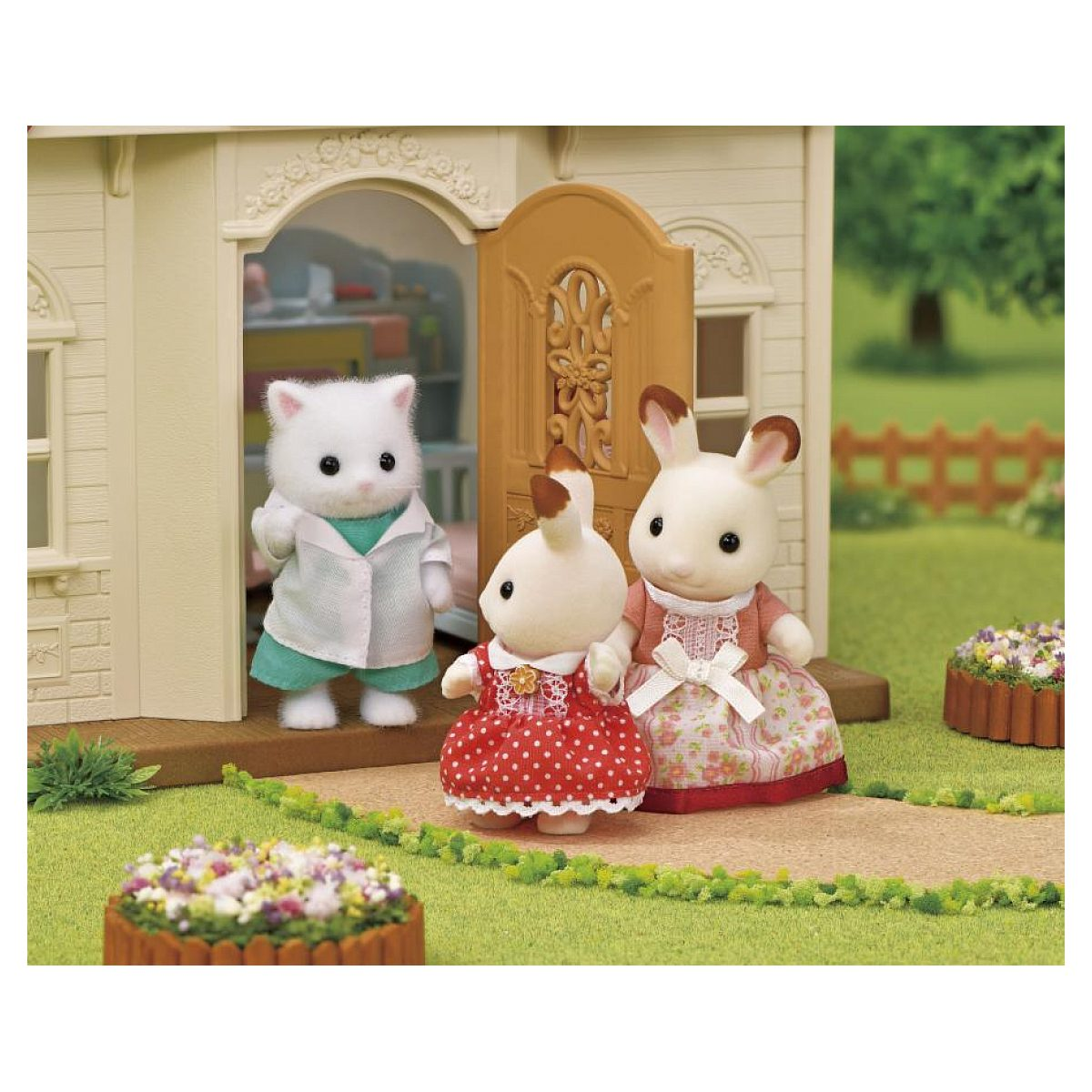 Figuras de juguete de un gato y dos conejos frente a una casa de muñecas en el césped.