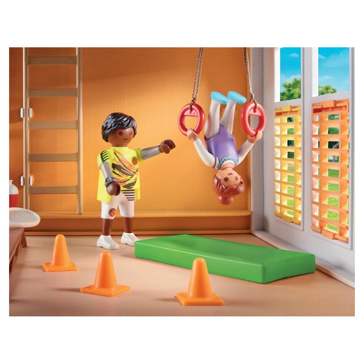 Playmobil-Figuren in einer Turnhalle, ein Kind turnt an Turnringen über einer grünen Matte.