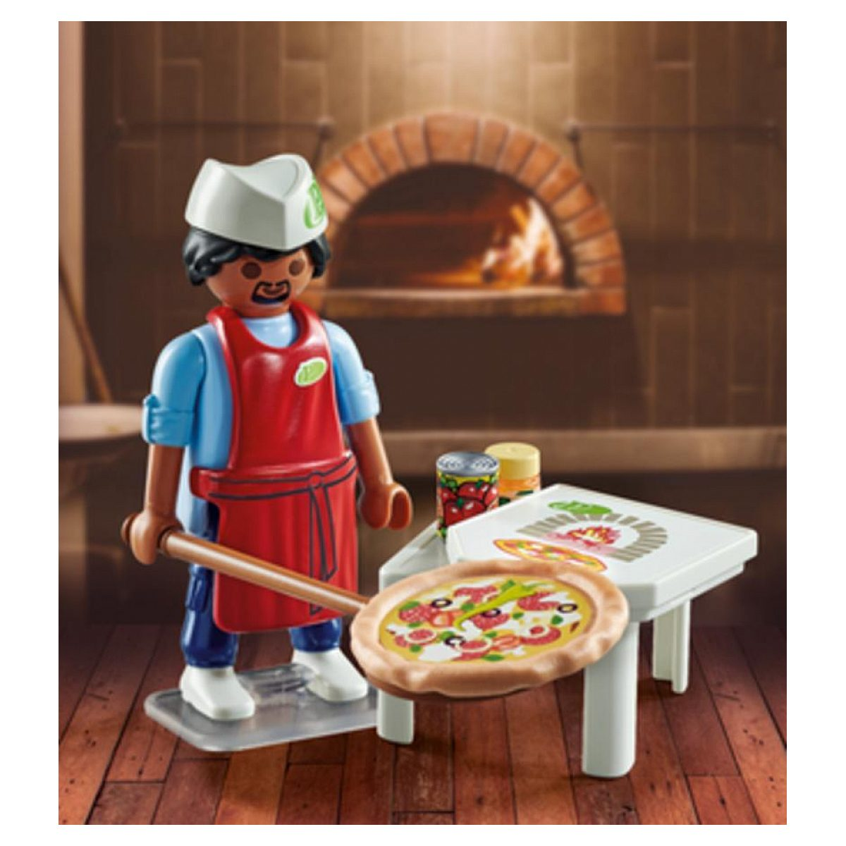 Playmobil-Pizzabäcker mit roter Schürze und weißer Mütze hält eine Pizza auf einer Schaufel vor einem Holzofen.