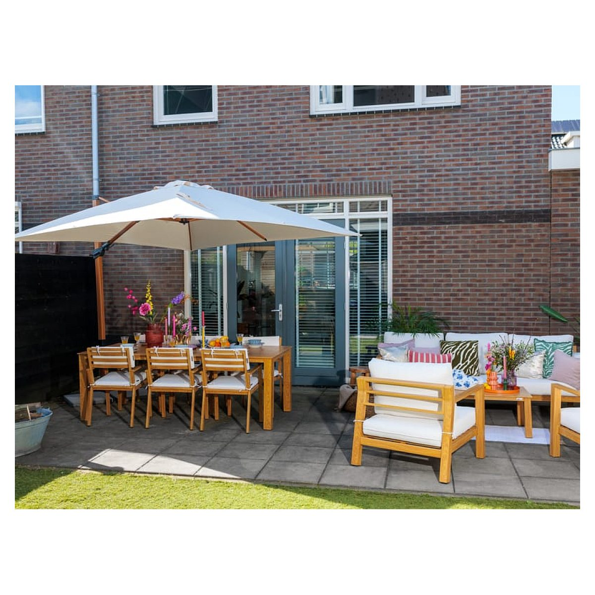 Eine gepflegte Terrasse mit Holzmöbeln, weißen Kissen, einem großen Sonnenschirm und einer roten Backsteinwand.