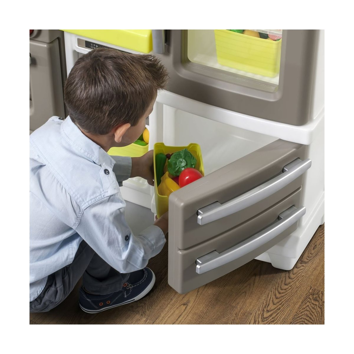 Ein Junge spielt mit einer Spielzeugküche und öffnet eine untere Schublade mit Plastikgemüse.