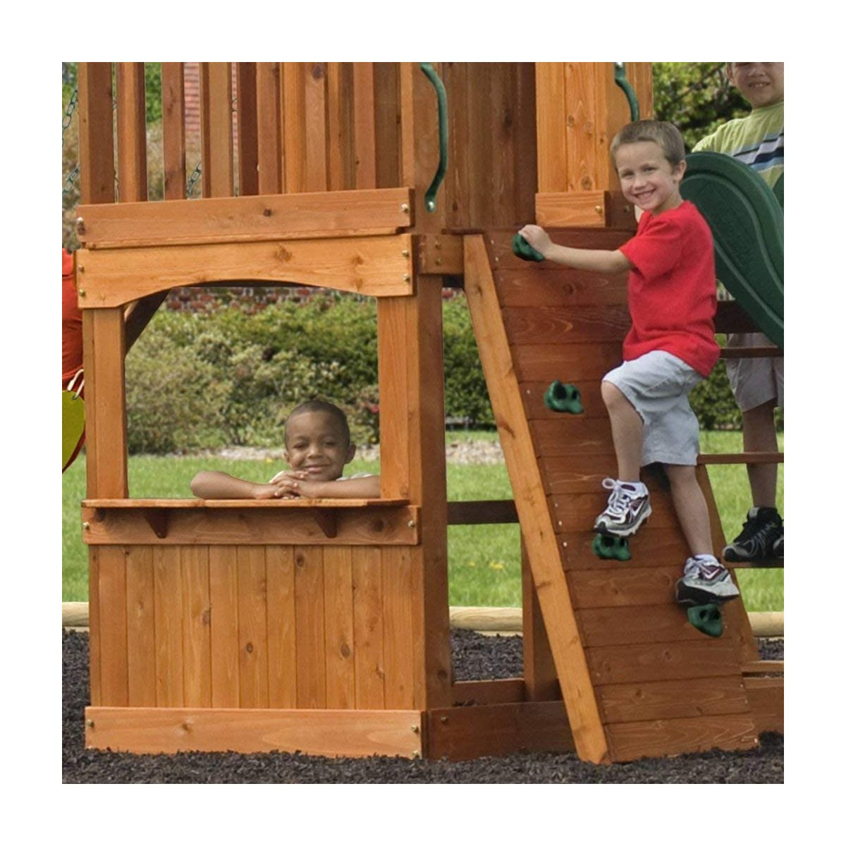 Kinder spielen auf einem hölzernen Spielplatz, einer klettert an der Wand hoch, ein anderer schaut aus dem Fenster.