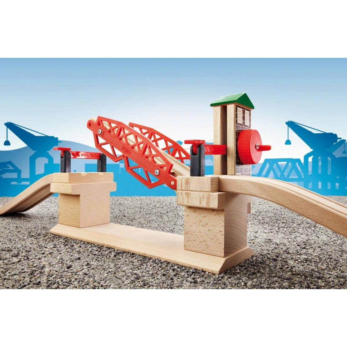 Eine hölzerne Spielzeug-Eisenbahnbrücke mit rotem Hebeteil und Kontrollturm vor einer blauen Hafenkulisse.