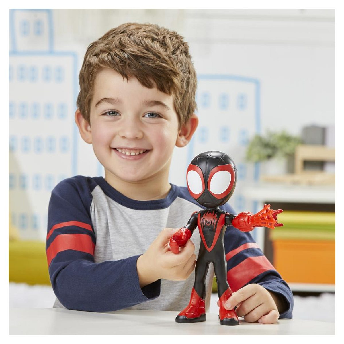Un niño sonríe mientras sostiene una figura de acción de Spider-Man negra y roja en una mesa blanca.