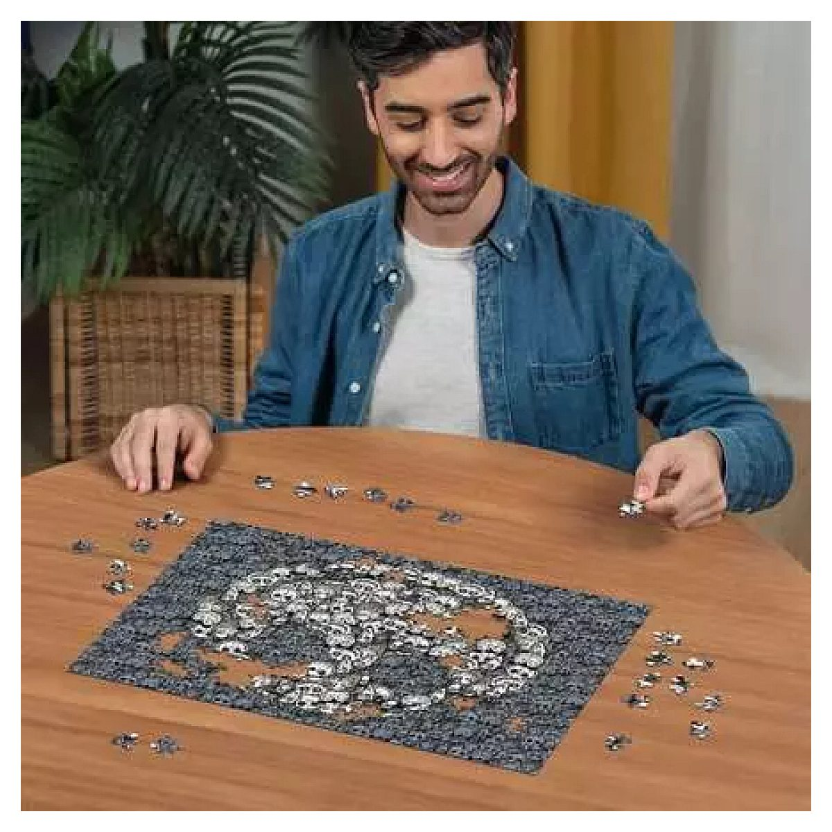 Ein lächelnder Mann sitzt an einem Holztisch und setzt ein komplexes graues Puzzle zusammen.