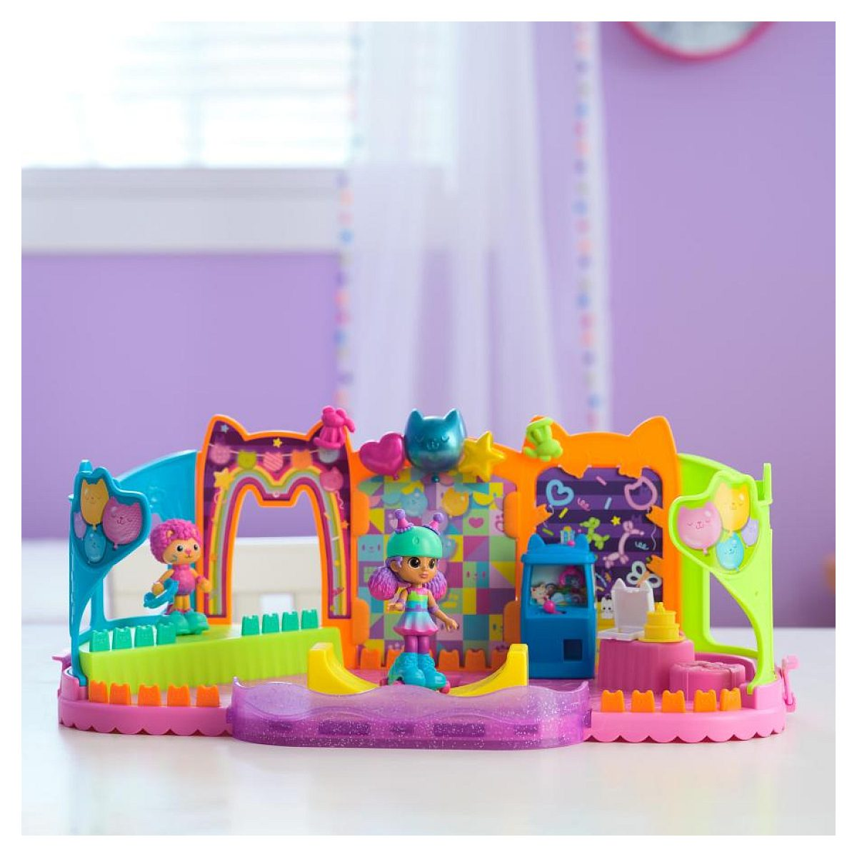 Buntes Puppenspielset mit kleinen Figuren und bunten Kulissen auf einem Tisch vor lila Wand.
