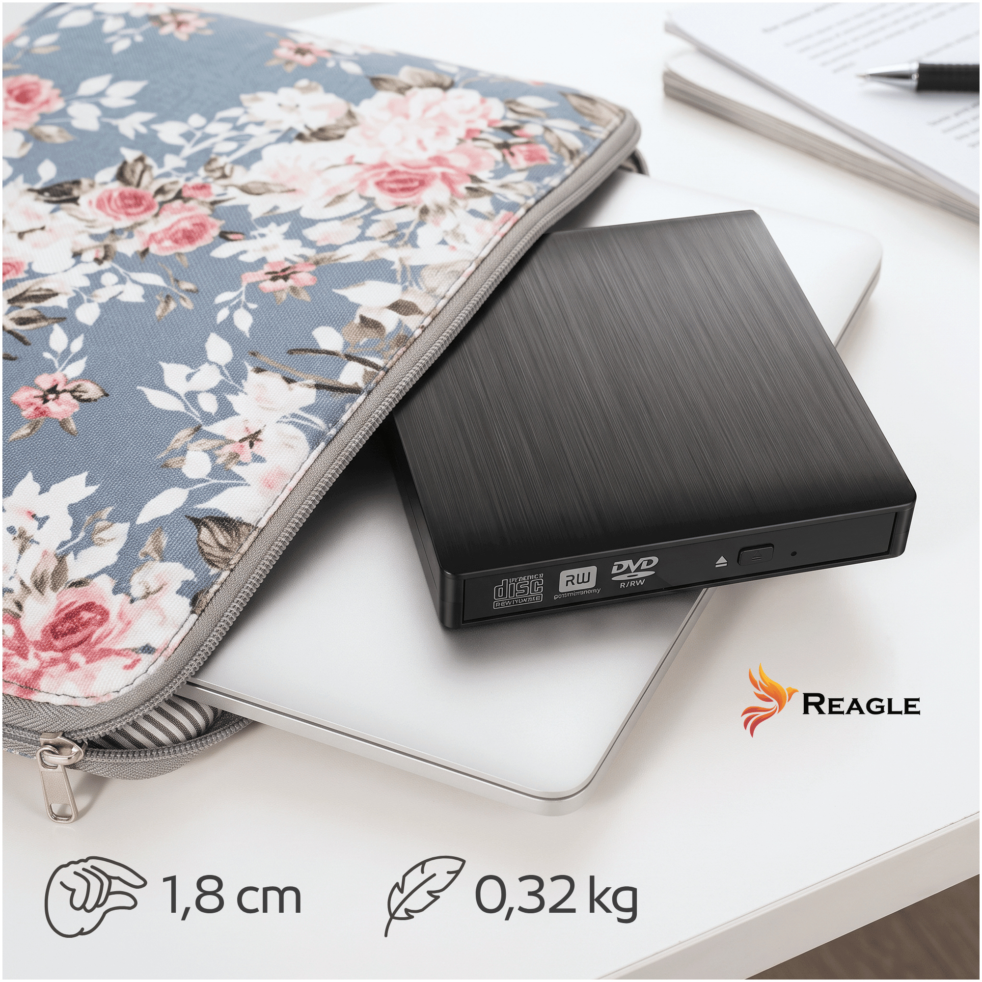 Ein schwarzes externes DVD-Laufwerk auf einem Laptop, neben einer blumigen Laptoptasche auf einem weißen Tisch.