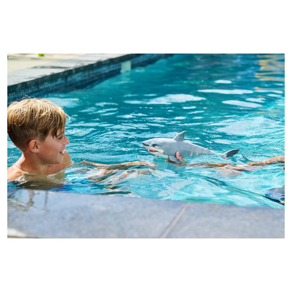 Un niño jugando con un tiburón de juguete en una piscina azul.