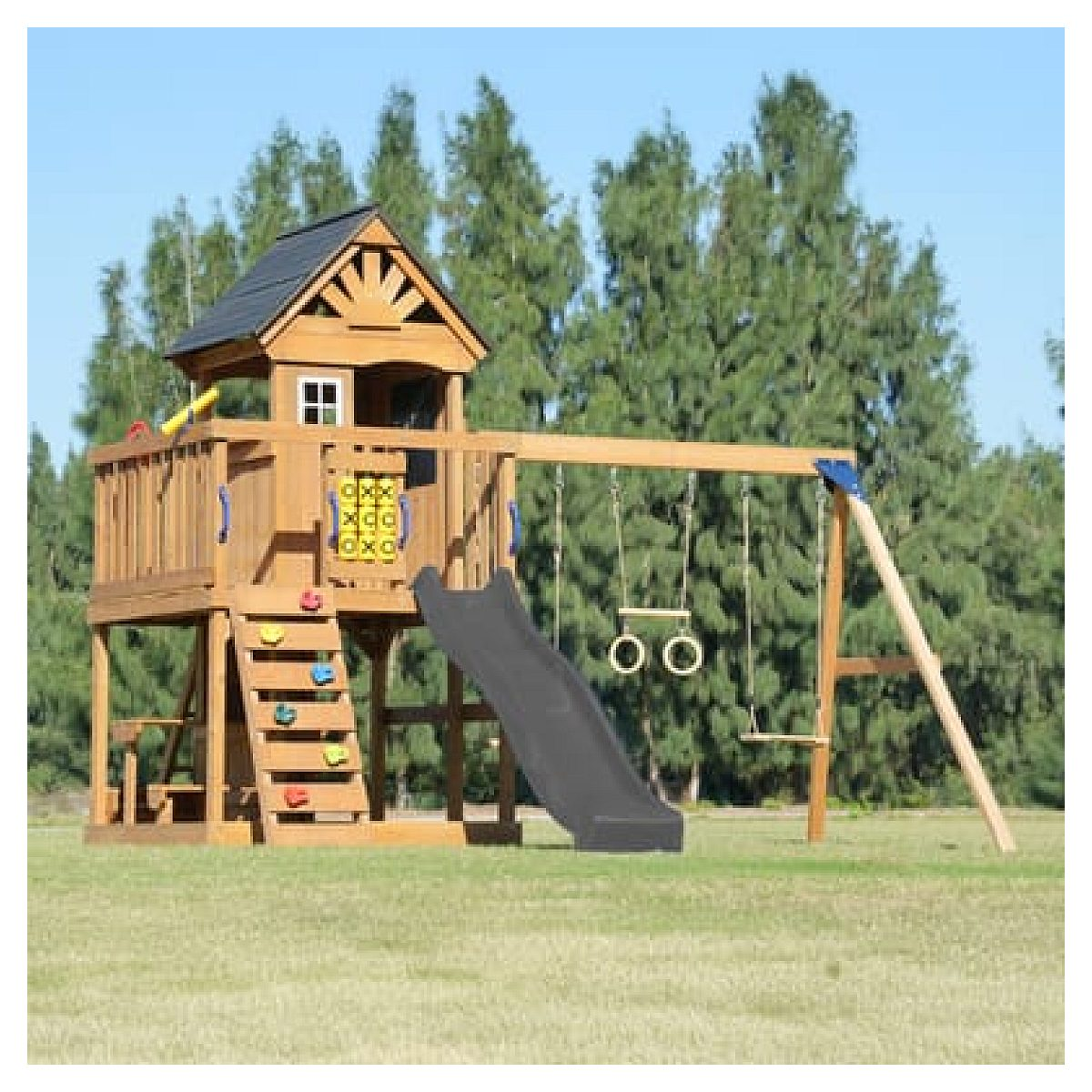 Ein Spielplatz aus Holz auf Wiese mit Spielhaus, schwarzer Rutsche, Kletterwand und Schaukeln vor Bäumen.