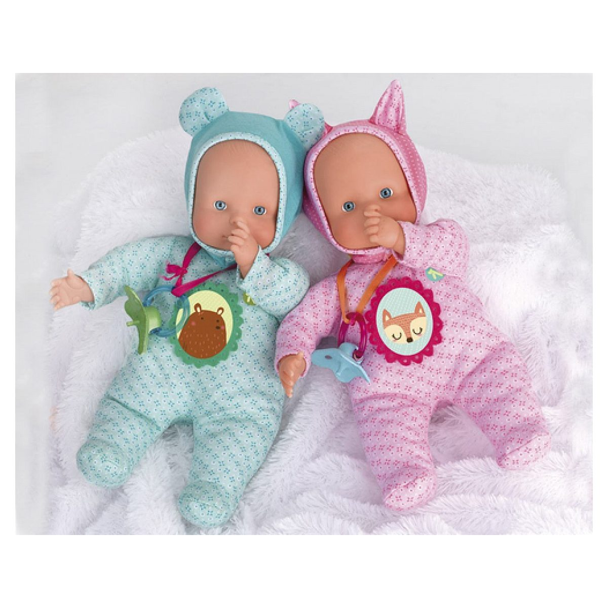 Zwei Babypuppen in blauen und rosa Anzügen mit Tierkapuzen liegen auf einer weißen Decke und nuckeln am Daumen.