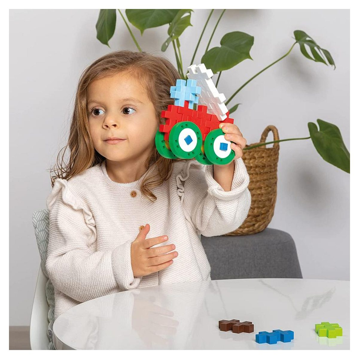 Una bambina tiene in mano un camion giocattolo di blocchi colorati seduta a un tavolo bianco.
