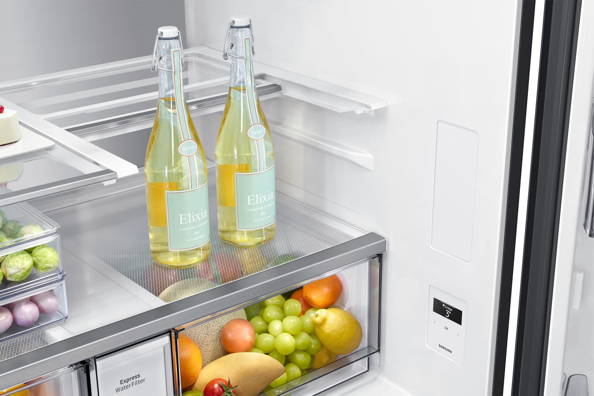 Geöffnter Kühlschrank mit zwei Flaschen Elixia-Limonade auf dem Regal und bunten Früchten im unteren Fach.