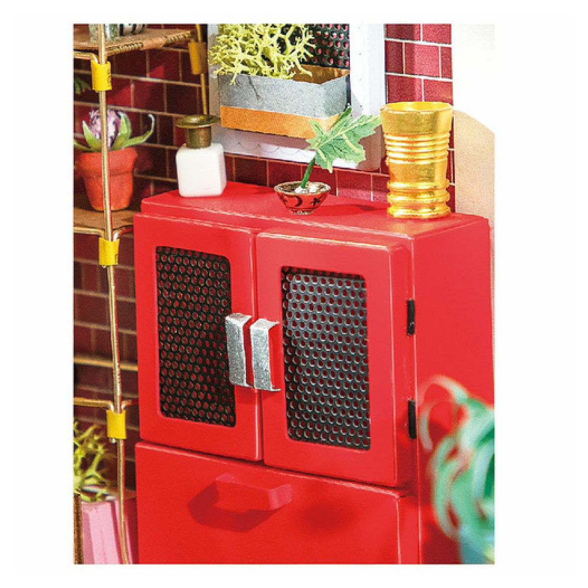 Un gabinete en miniatura rojo con puerta de malla sostiene pequeños objetos decorativos.
