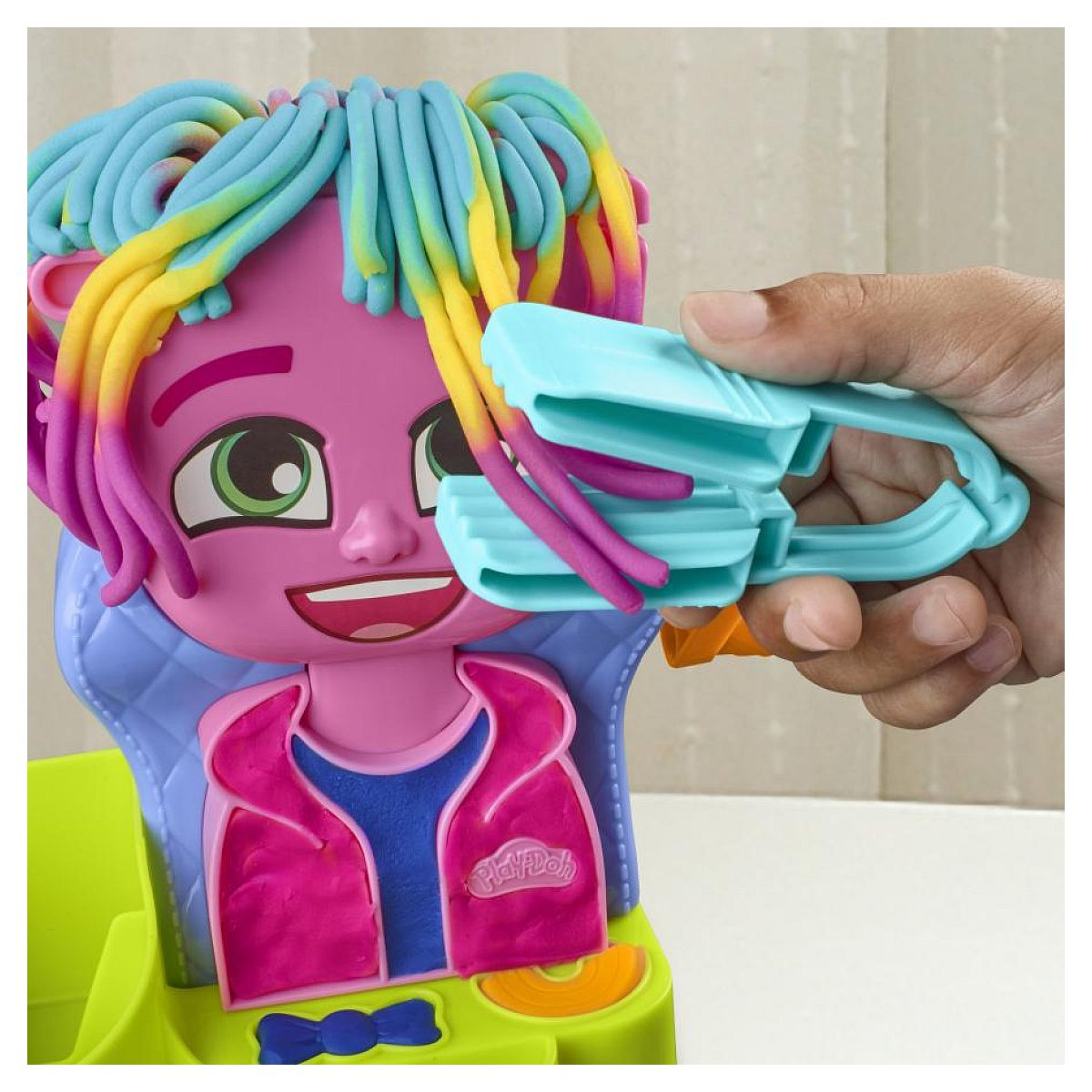 Una mano usa una herramienta azul para peinar cabello de plastilina colorido en un juguete rosa.