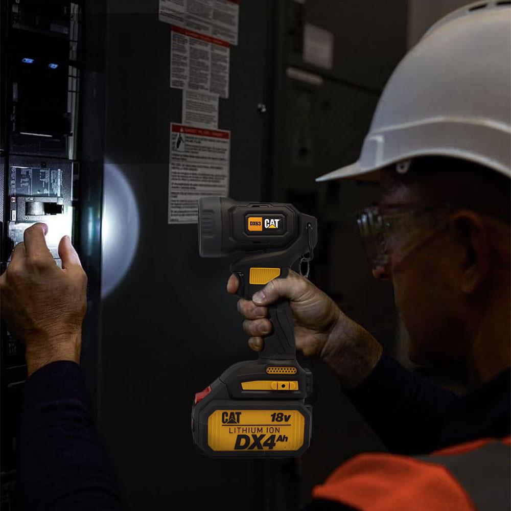 Baretli bir işçi Cat şarjlı çalışma lambasını tutarak elektrik panosunu inceliyor.