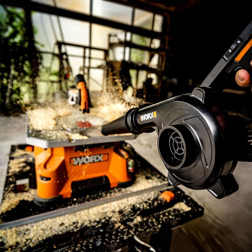 Un souffleur de feuilles Worx noir nettoie la sciure d'un établi orange dans un atelier.