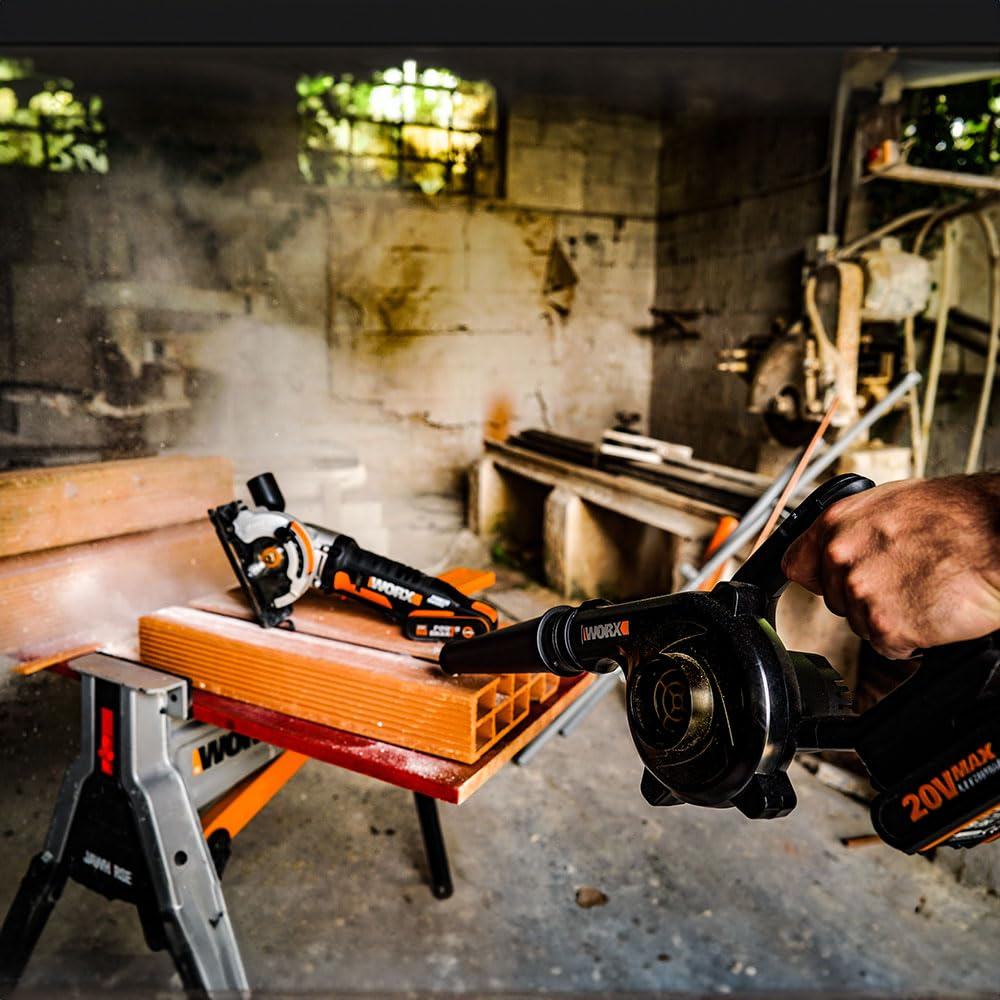 Une main tient un souffleur Worx dans un atelier avec scie à bois et établis.